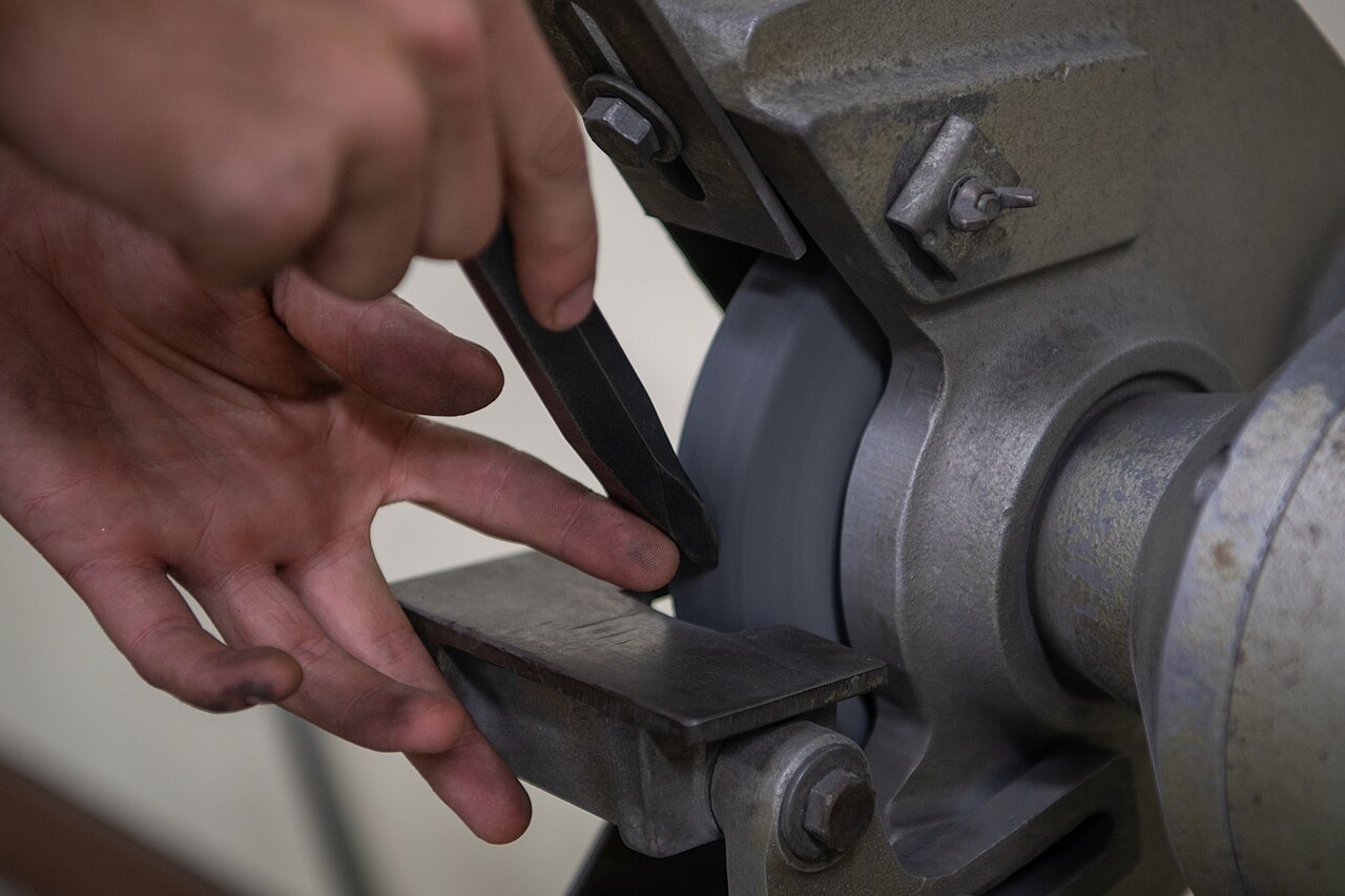 A worker deburring a metal part with sparks coming from the edge
