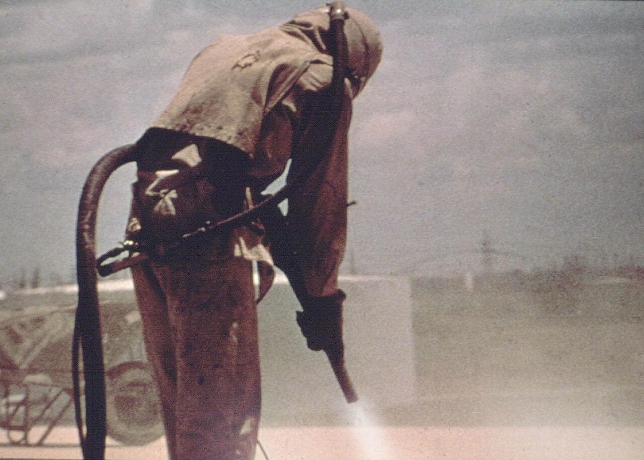 A worker wearing full protective gear while sandblasting
